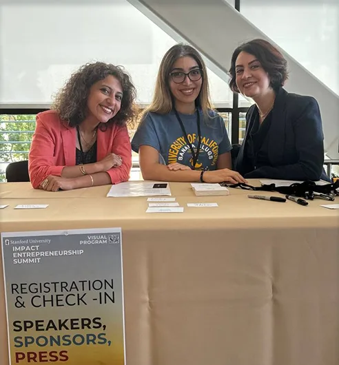 Three volunteers at the registration and check-in desk of a Stanford entrepreneurship summit.